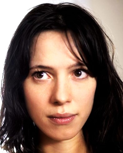 Close-up portrait of a woman with dark hair and a neutral expression, looking toward the camera.